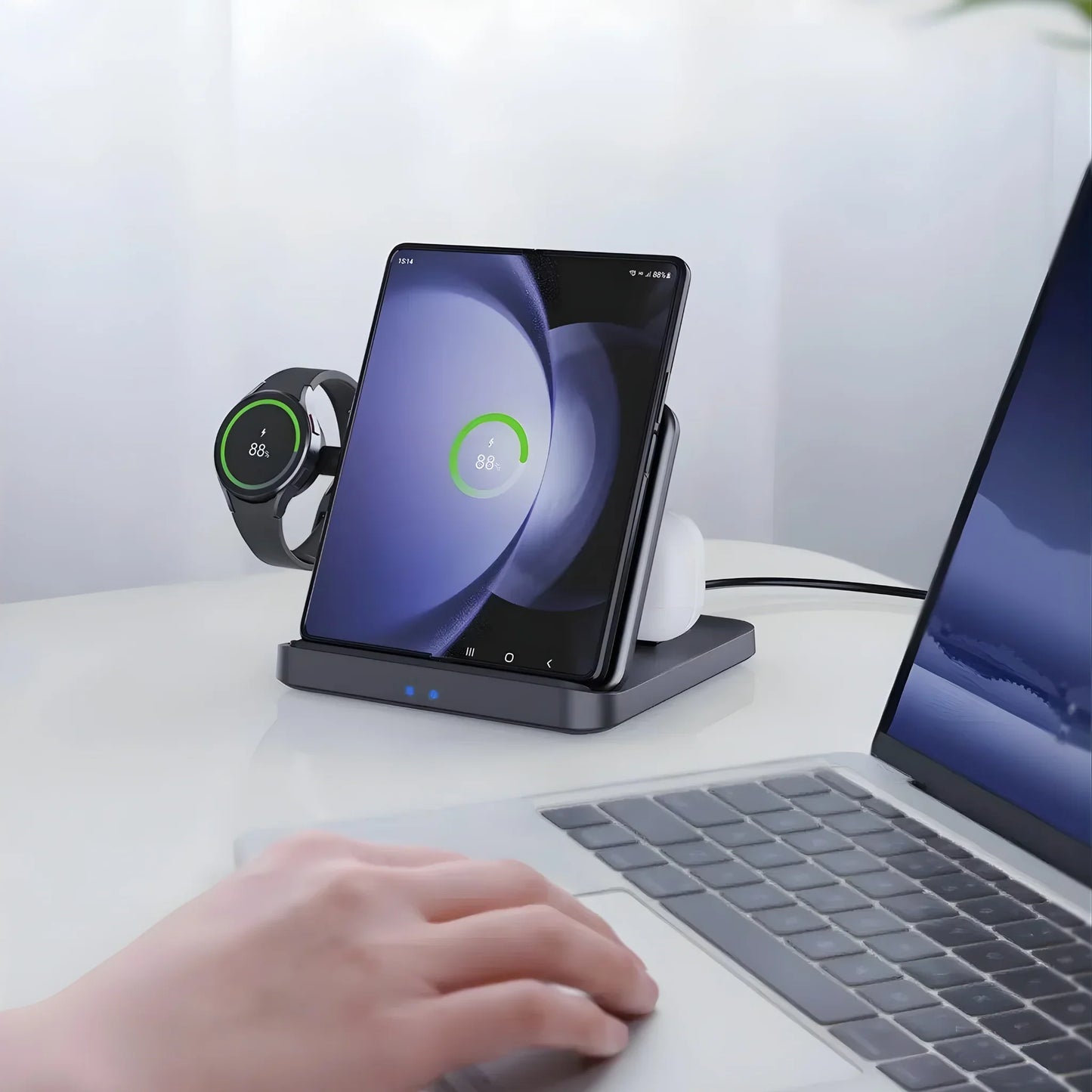 Wireless charging station powering foldable smartphone and smartwatch on white desk near laptop