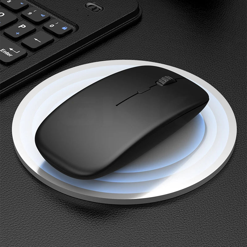 Black wireless mouse on a round white mouse pad with a keyboard in the background.